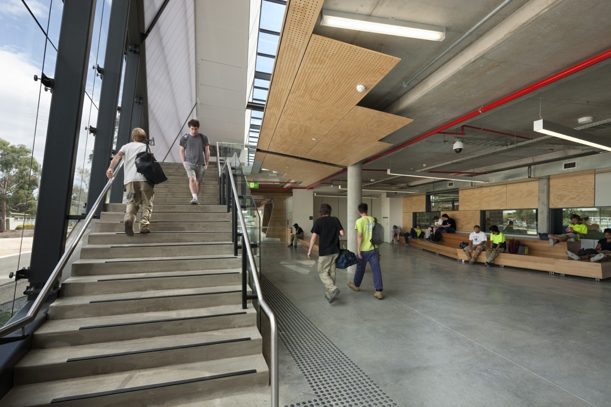 Students walking through the light-filled foyer of VU Sunshine Campus, with others seated on tiered timber benches