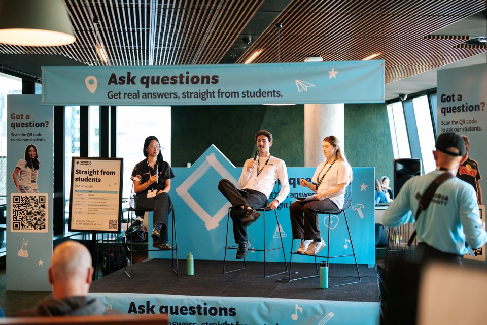 A panel of three student hosts sits on stools under an “Ask questions” banner at VU City Tower.