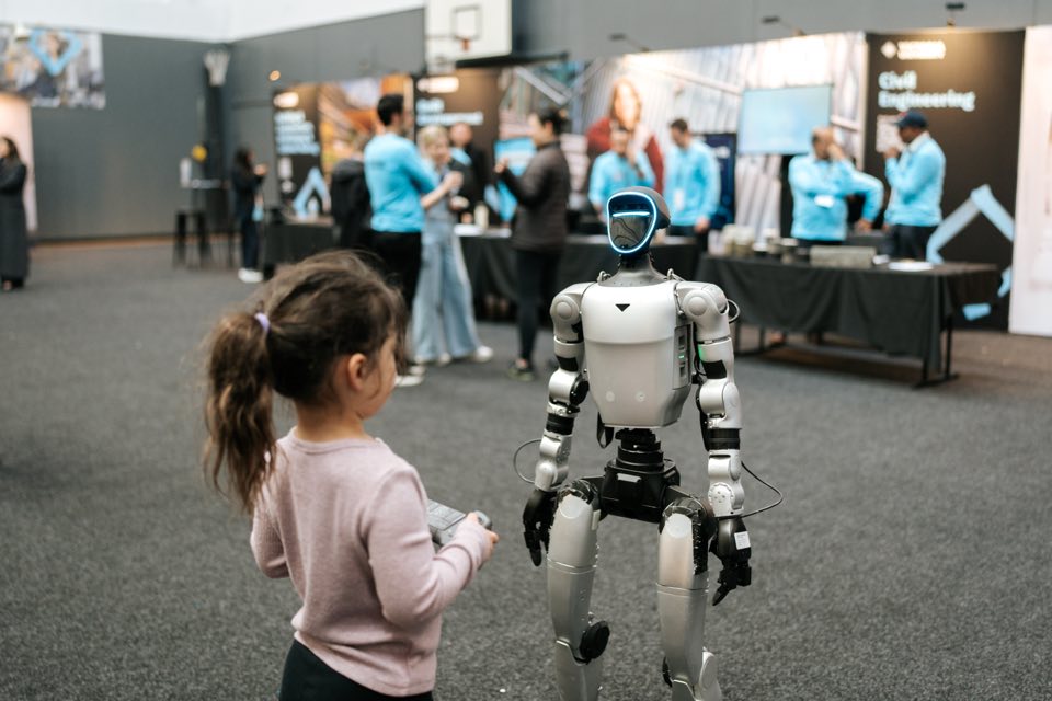 A young girl uses a handset to move a humanoid robot at the engineering stand.