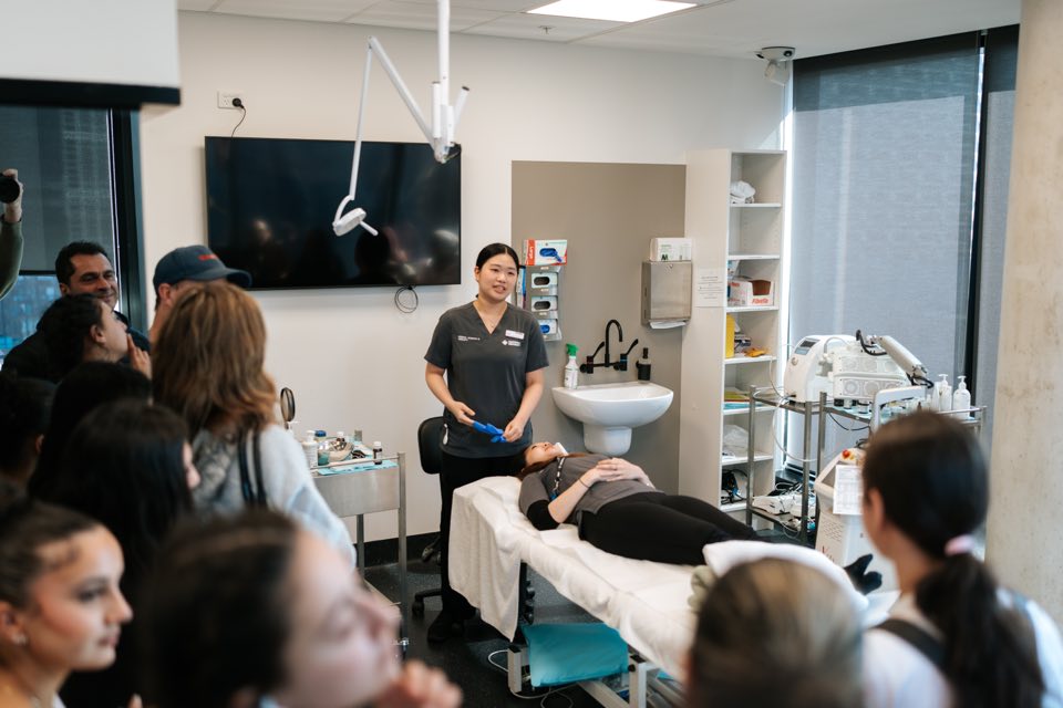 A dermal science student demonstrates a skin treatment to a room packed with visitors.