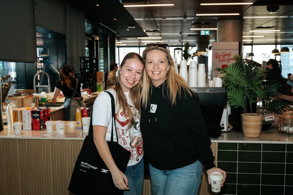 A prospective student and her mum smile together at the campus café, coffee in hand.
